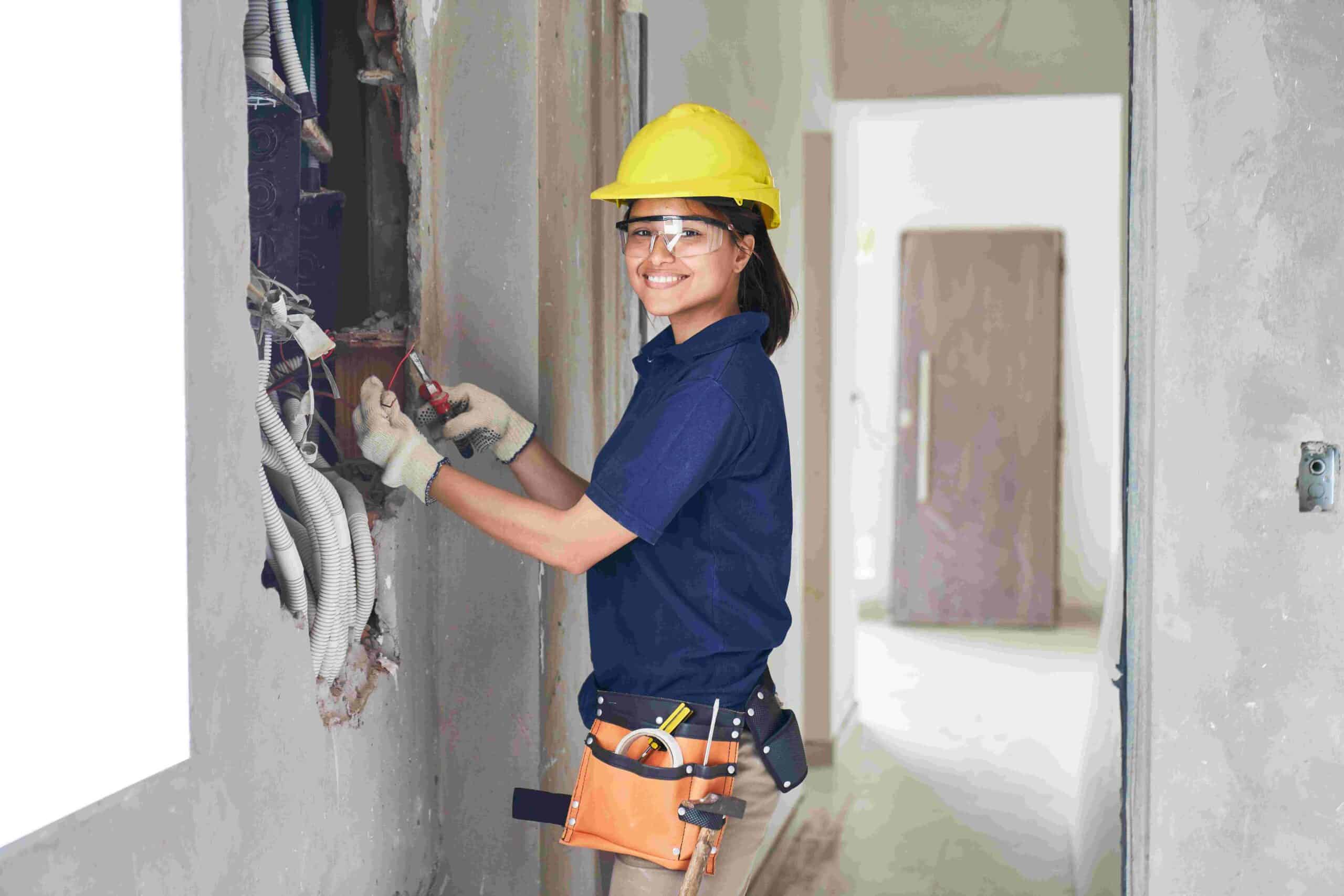 A lady electrician smiling and fixing an electrical issue with a plier on her hand holding a wire